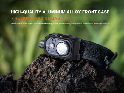 Black Fenix HL45R Headlamp on a rock with greenery in the background, highlighting high-quality aluminum alloy front case.